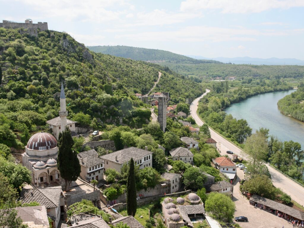 "Mosque minaret rising above a traditional Balkan town surrounded by green hills